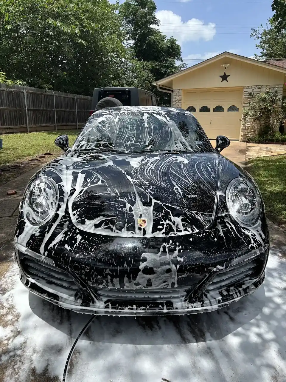 Black sports car covered in foam during an exterior wash