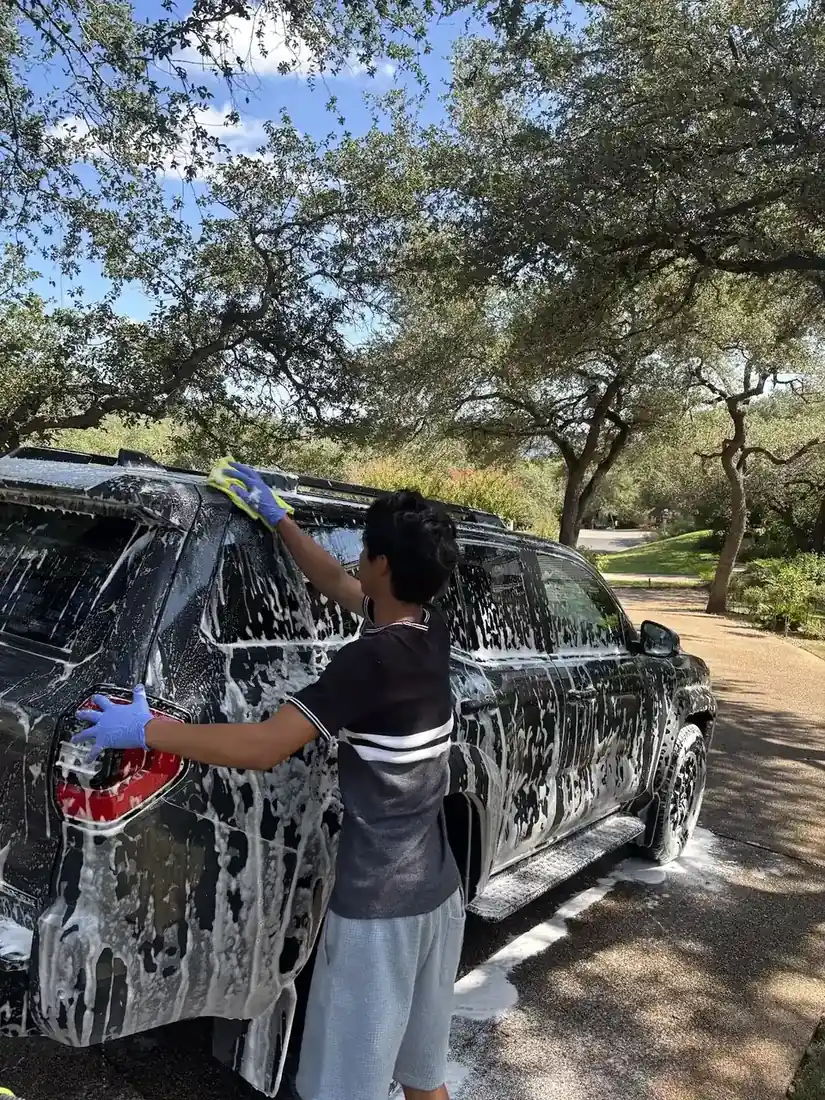 Detailer hand washing a foam-covered SUV with a wash mitt